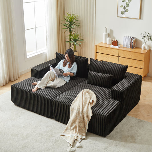 Black corduroy sectional sofa with plush cushions and a woman relaxing on it