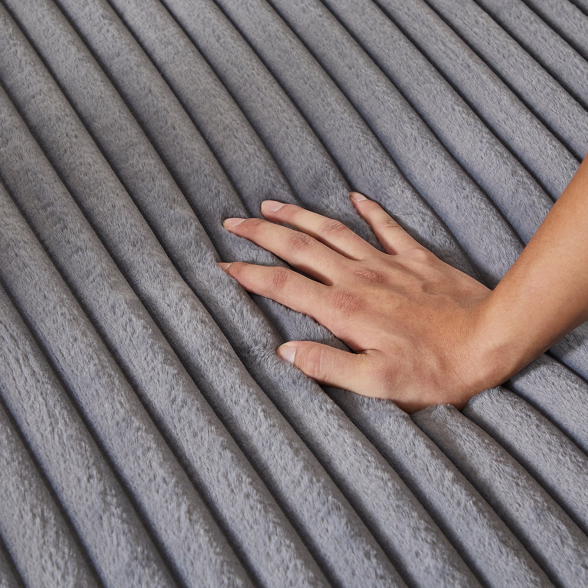Closeup of a hand sinking into a plush grey ribbed blanket showing softness