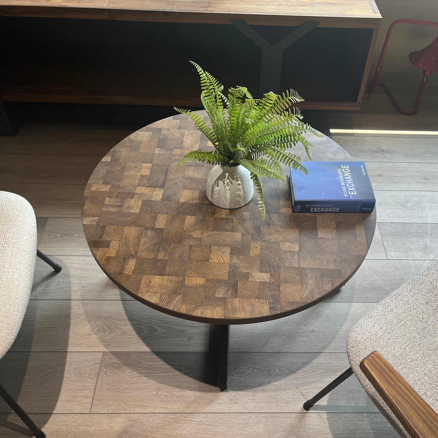 Round oak wood end table with a patchwork design featuring a white vase with ferns and a book