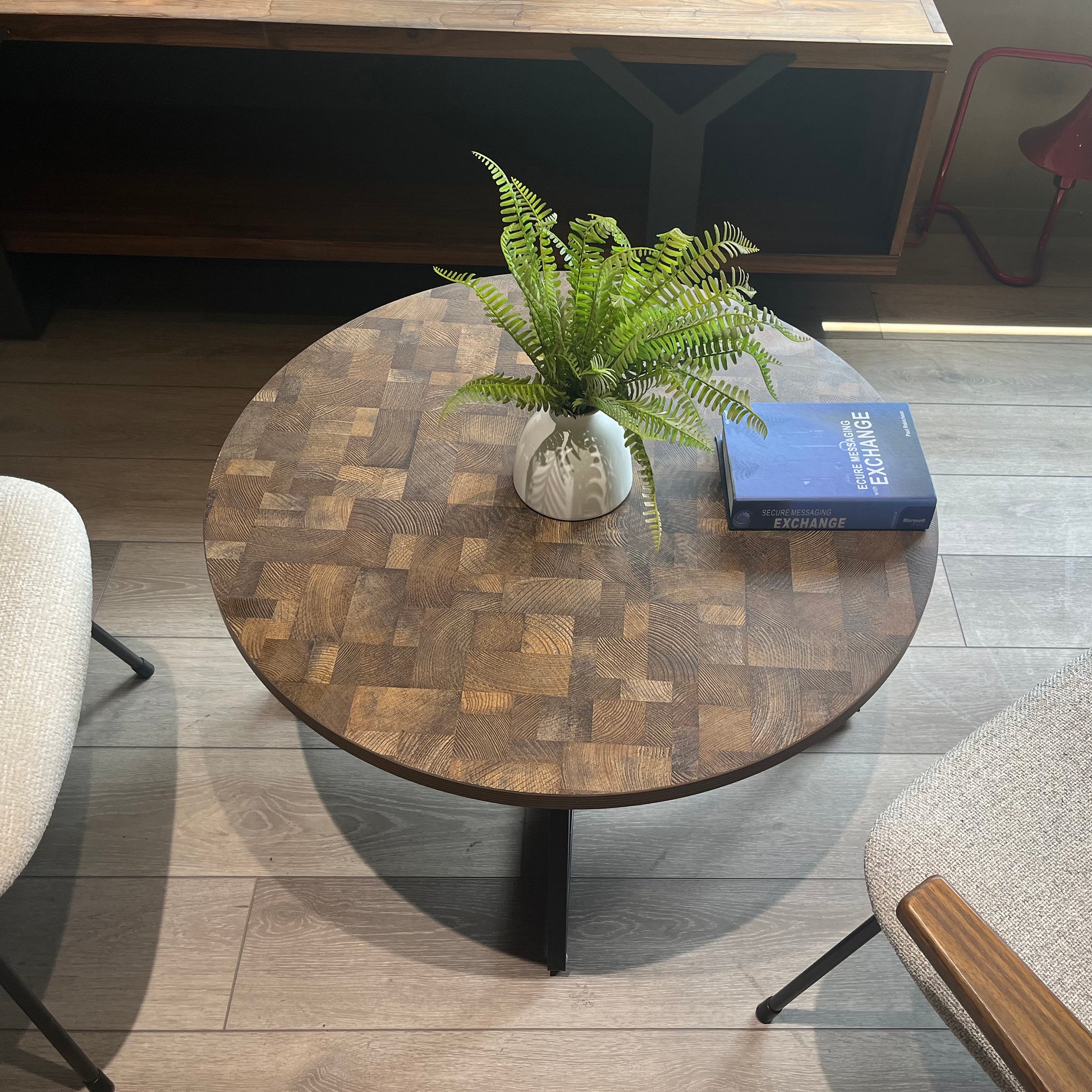Round oak wood end table with a patchwork design featuring a white vase with ferns and a book