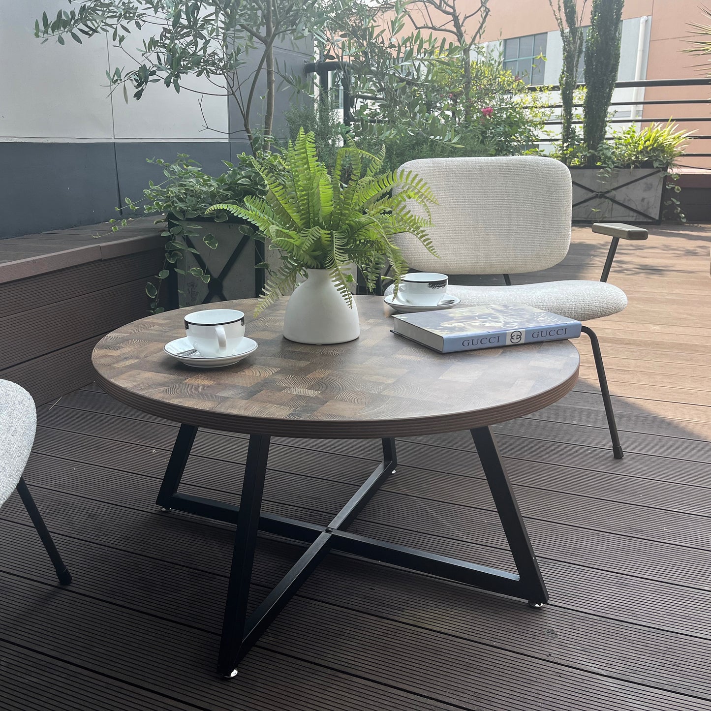 Round wooden coffee table with black metal legs and a faux fern arrangement