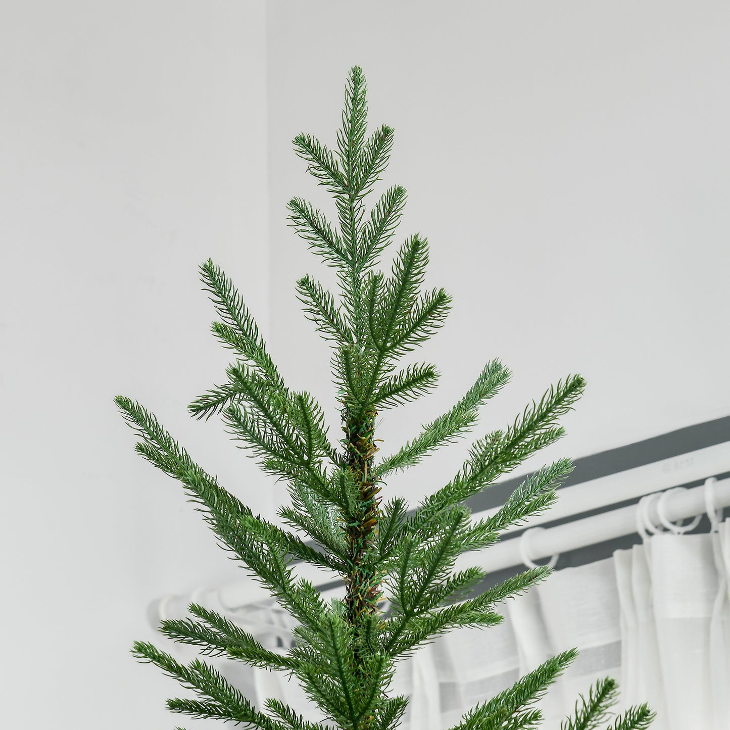 Closeup of a lush green artificial christmas tree top with detailed needles and a visible trunk