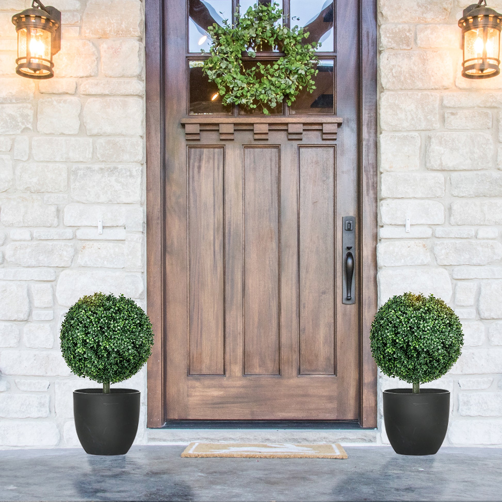 Pair of artificial boxwood topiary balls in black pots flanking a wooden door
