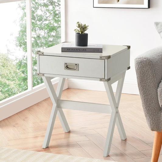 White campaign end table with drawer and silver hardware beside a grey armchair