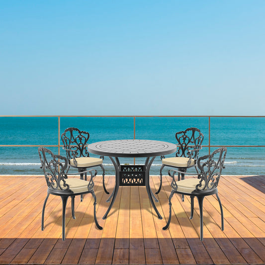 Black cast iron bistro set with decorative scrollwork chairs and mosaic tabletop on wooden deck overlooking the ocean