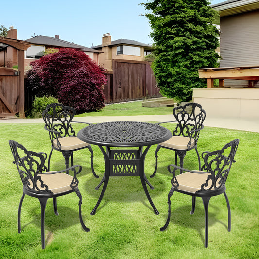 Black cast aluminum patio dining set with ornate scrollwork chairs and round table on green grass
