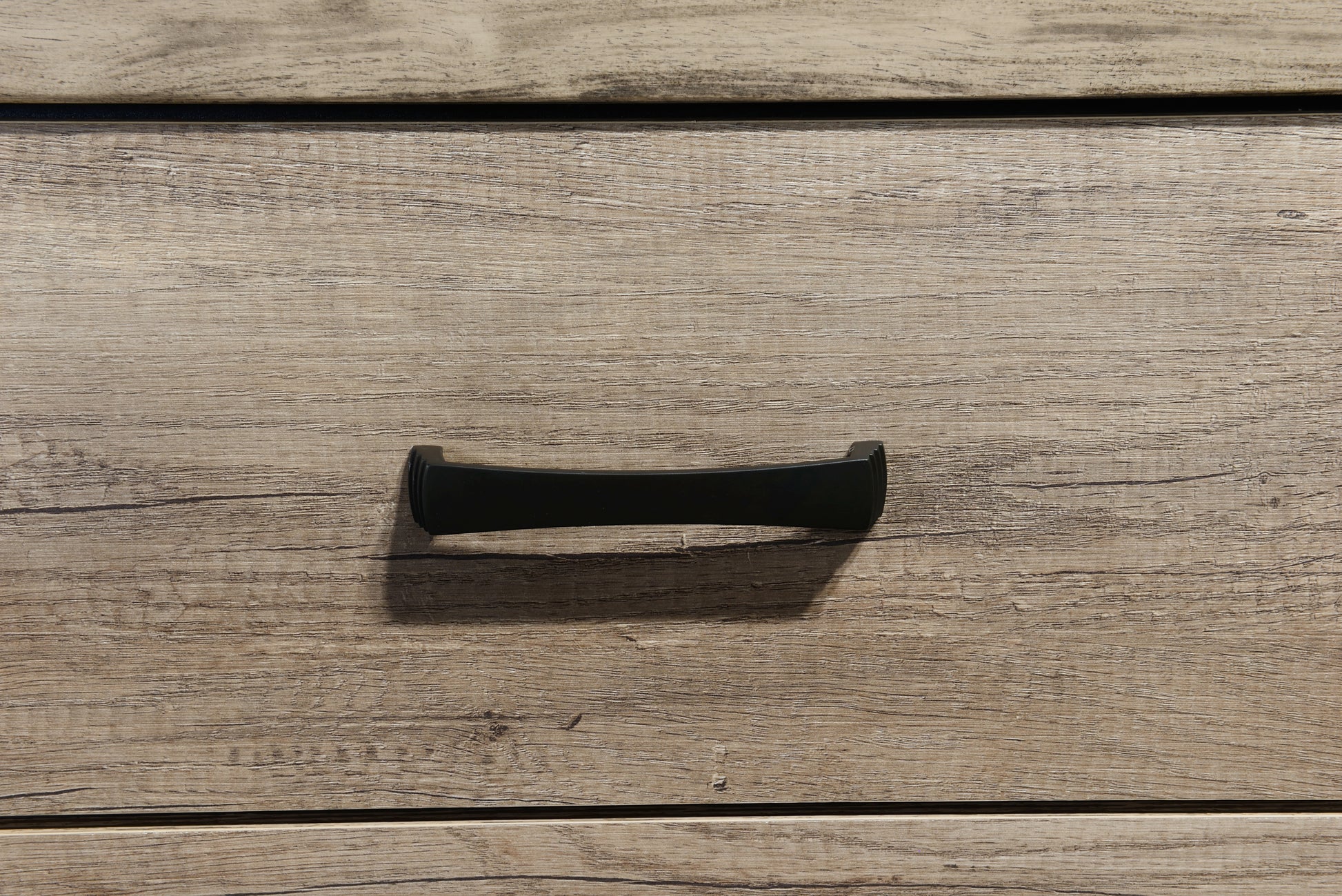 Black curved drawer pull on light wood grain dresser drawer