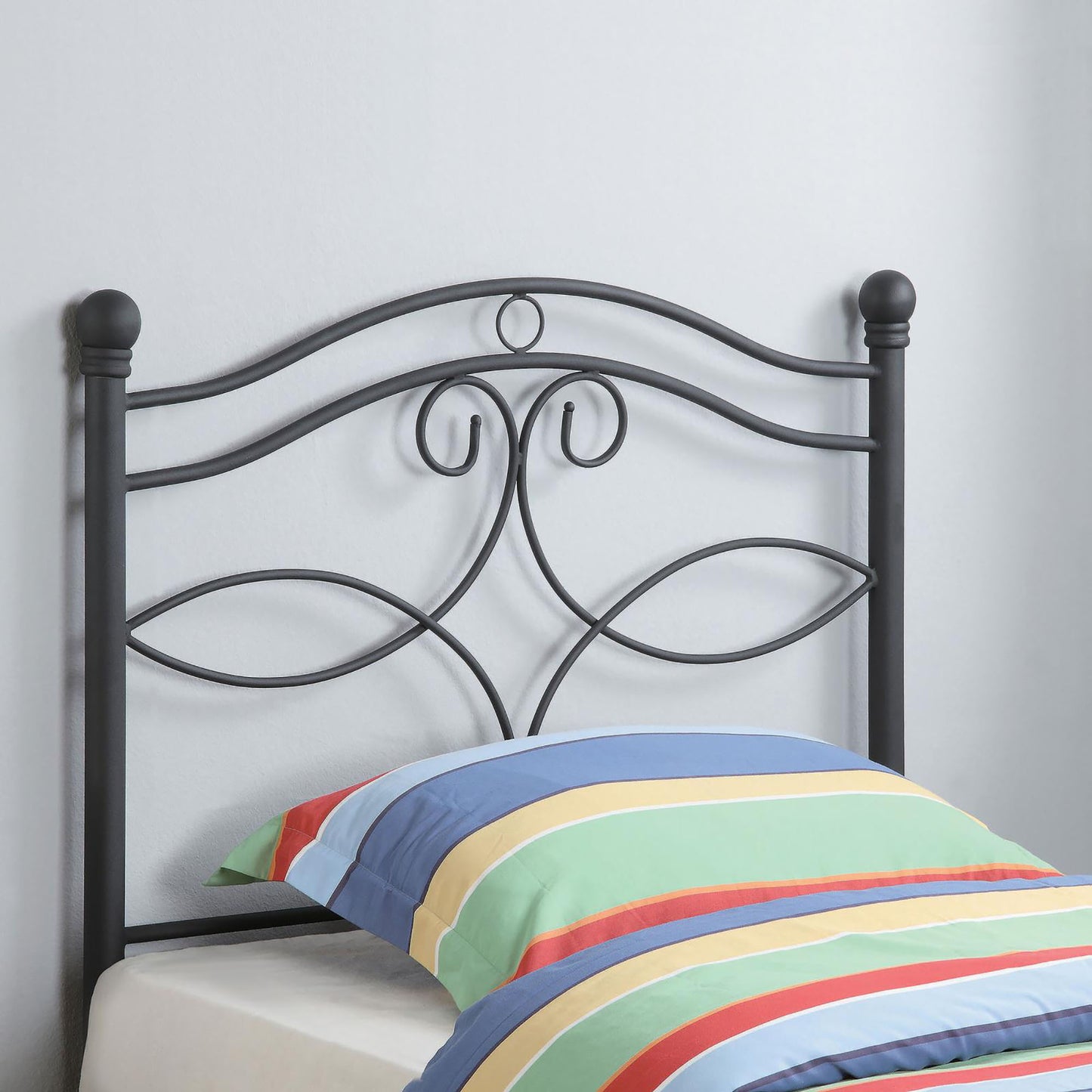 Black metal headboard with ornate scrollwork and finials complementing a striped pillow