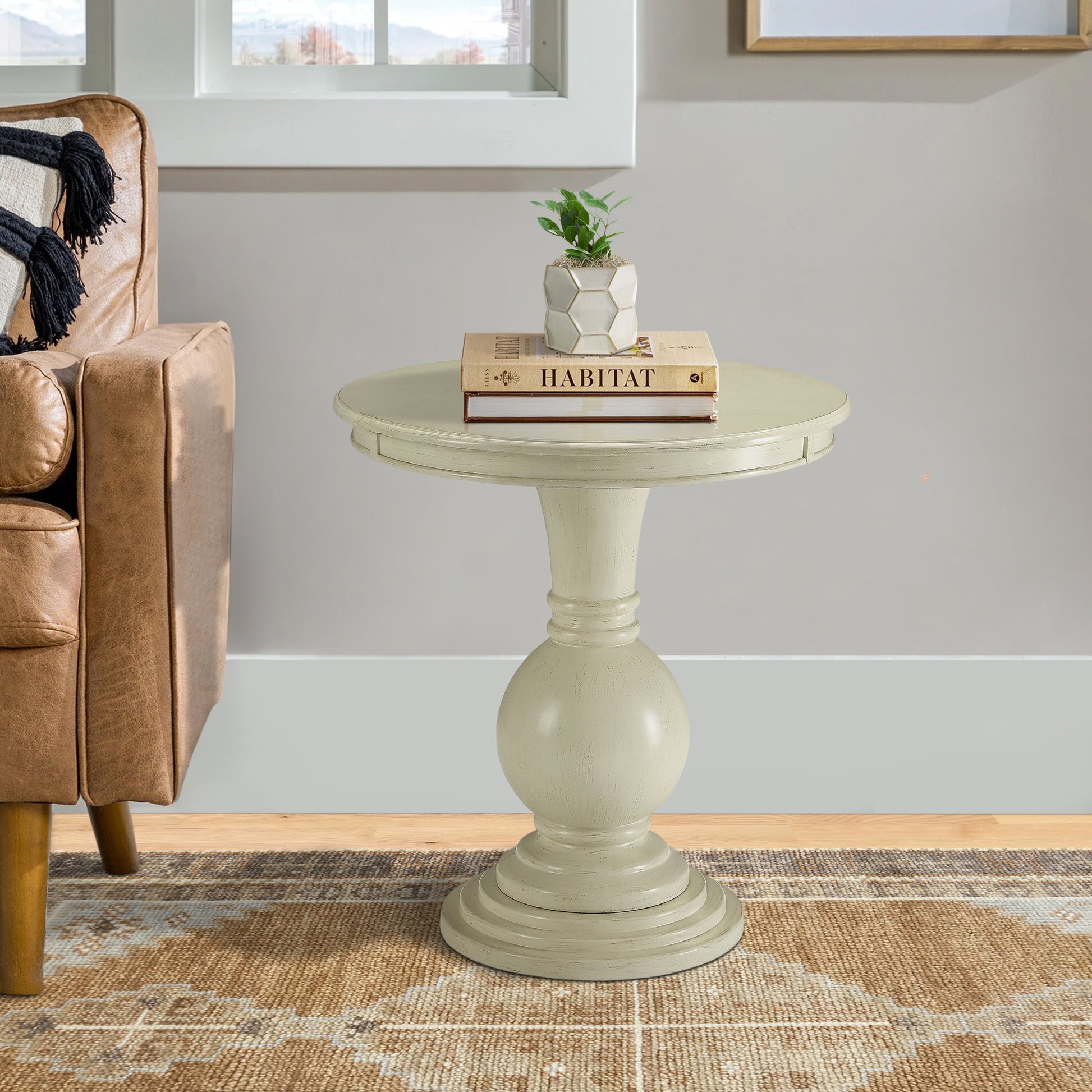 Cream pedestal accent table with stacked books and plant