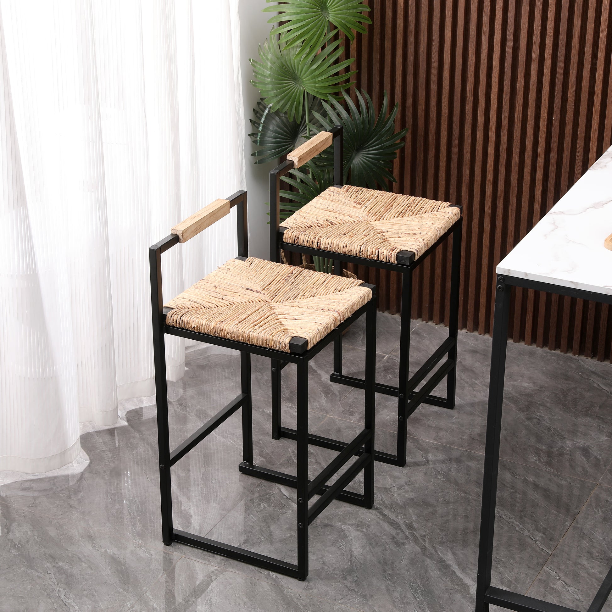 Two black metal bar stools with natural woven seats and wooden armrests sit near a marbletopped table