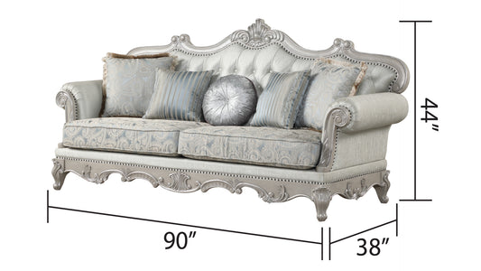 Ornate silver carved sofa with tufted light blue upholstery and patterned throw pillows