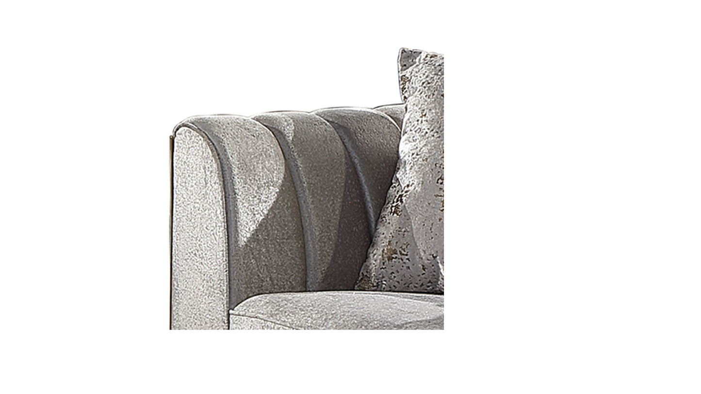 Closeup of a plush grey velvet armchair with button tufting and a decorative pillow