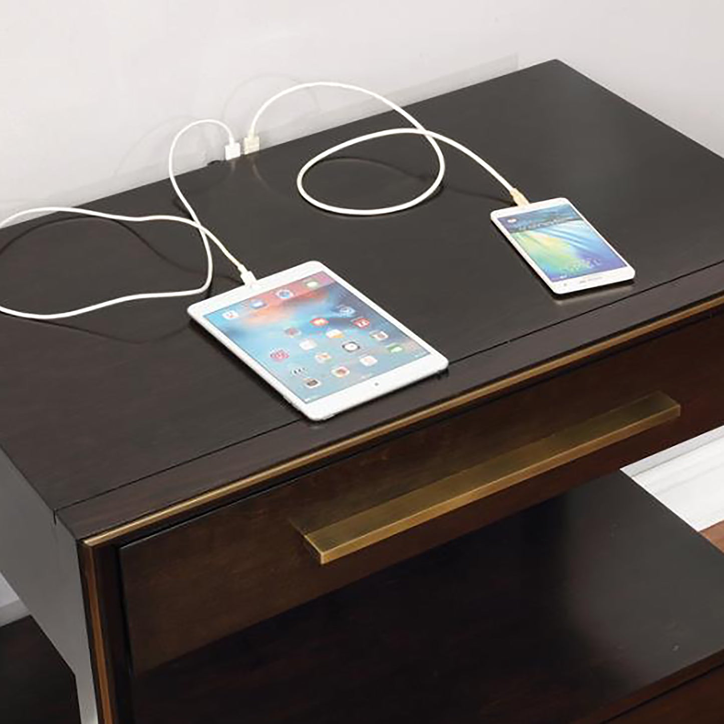 White tablet and smartphone charging on a dark wood nightstand