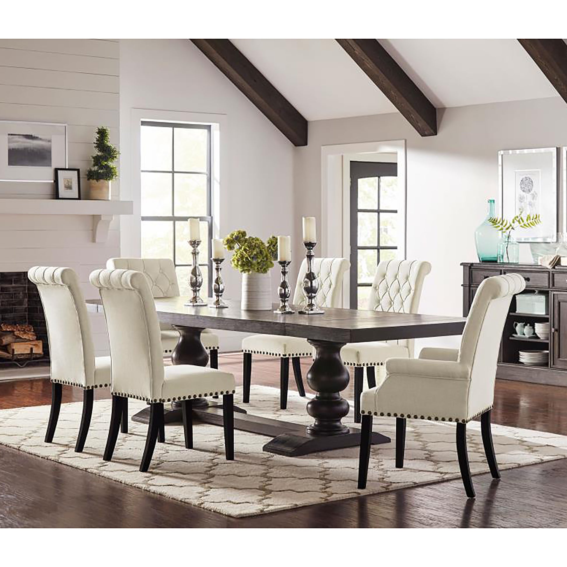 Tufted cream dining chairs with nailhead trim surrounding a dark wood pedestal dining table