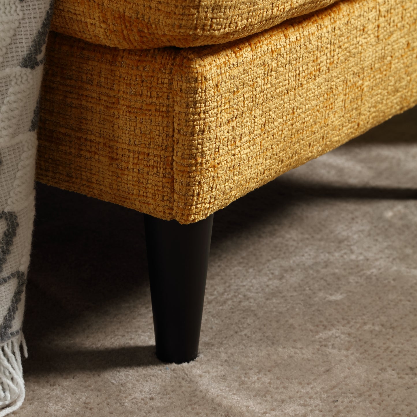 Textured mustard yellow couch fabric with dark tapered leg on carpet