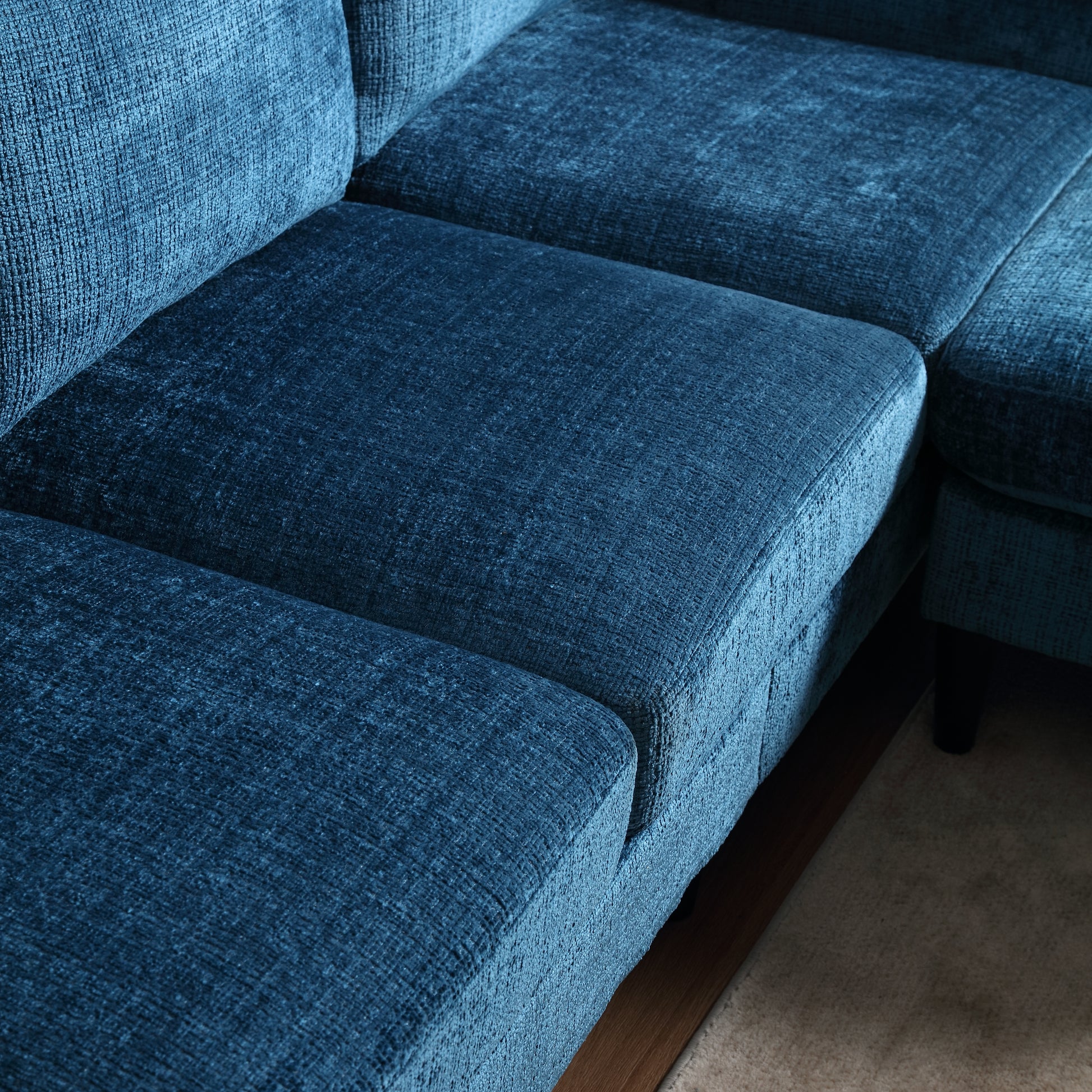 Closeup of a deep teal velvet sectional sofa with plush cushions and a textured fabric