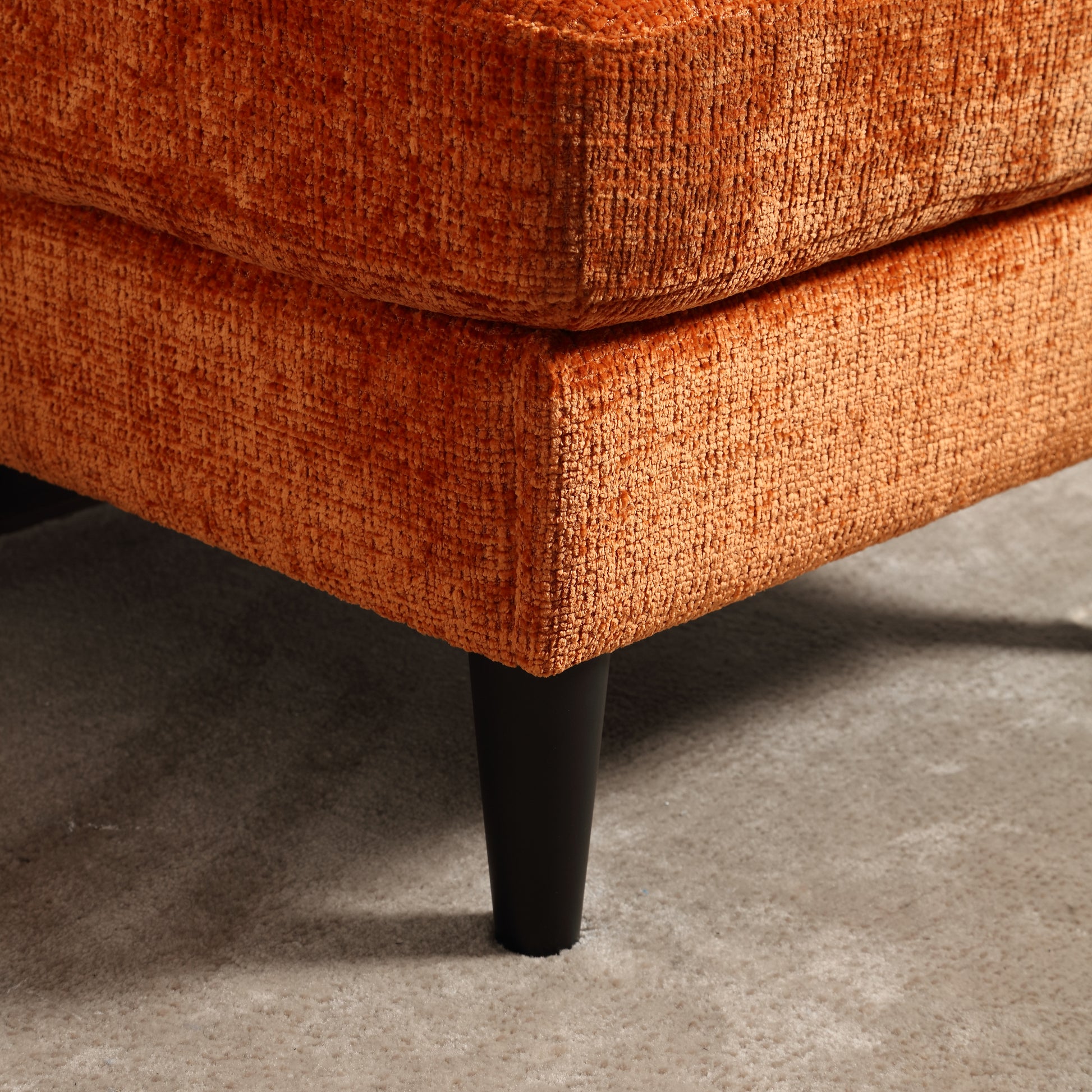 Rich burnt orange velvet upholstery on a modern sofa corner with dark wood legs