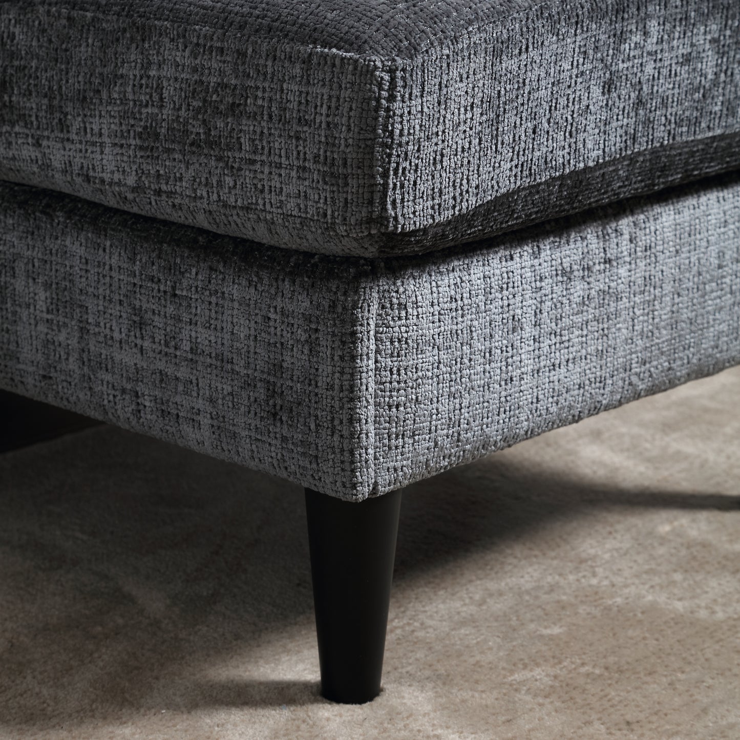 Closeup of dark gray textured fabric on a sofa corner with black tapered legs