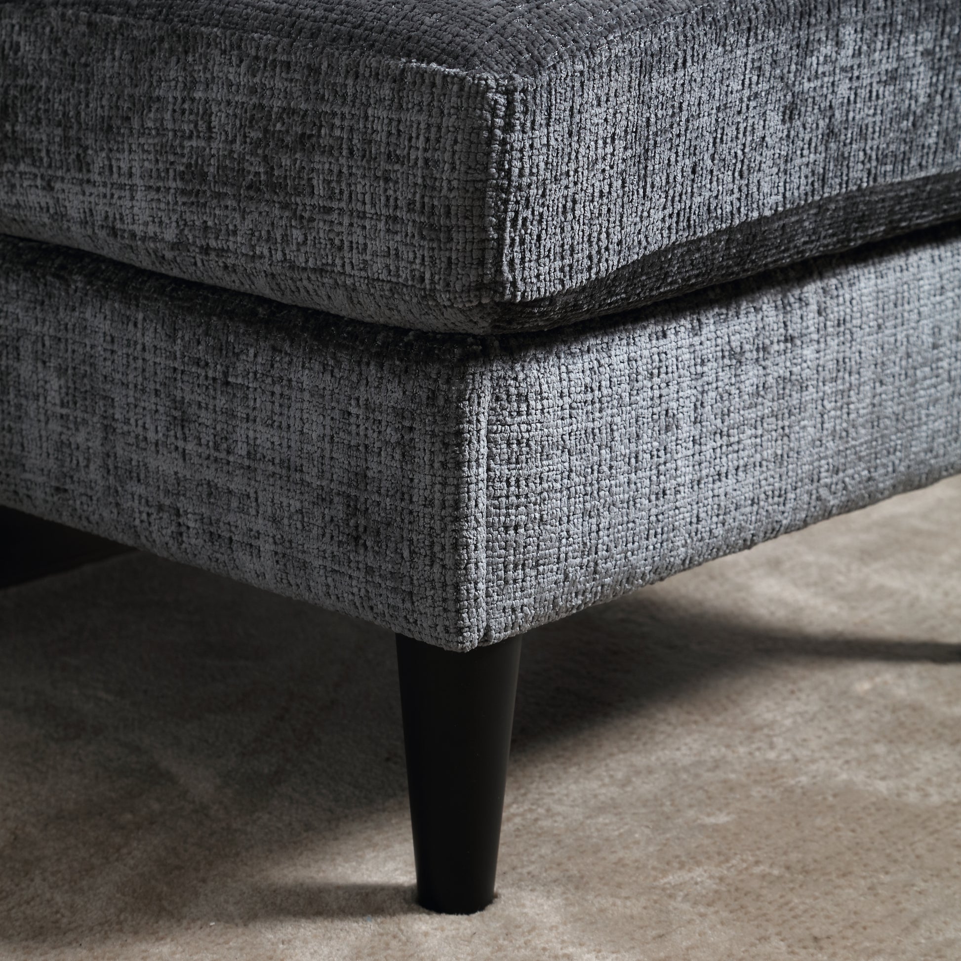 Closeup of dark gray textured fabric on a sofa corner with black tapered legs