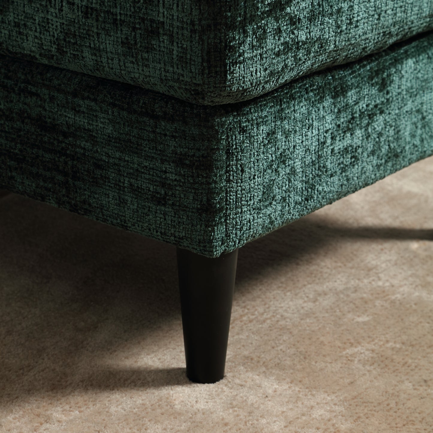 Teal velvet sofa corner with black tapered leg on beige carpet