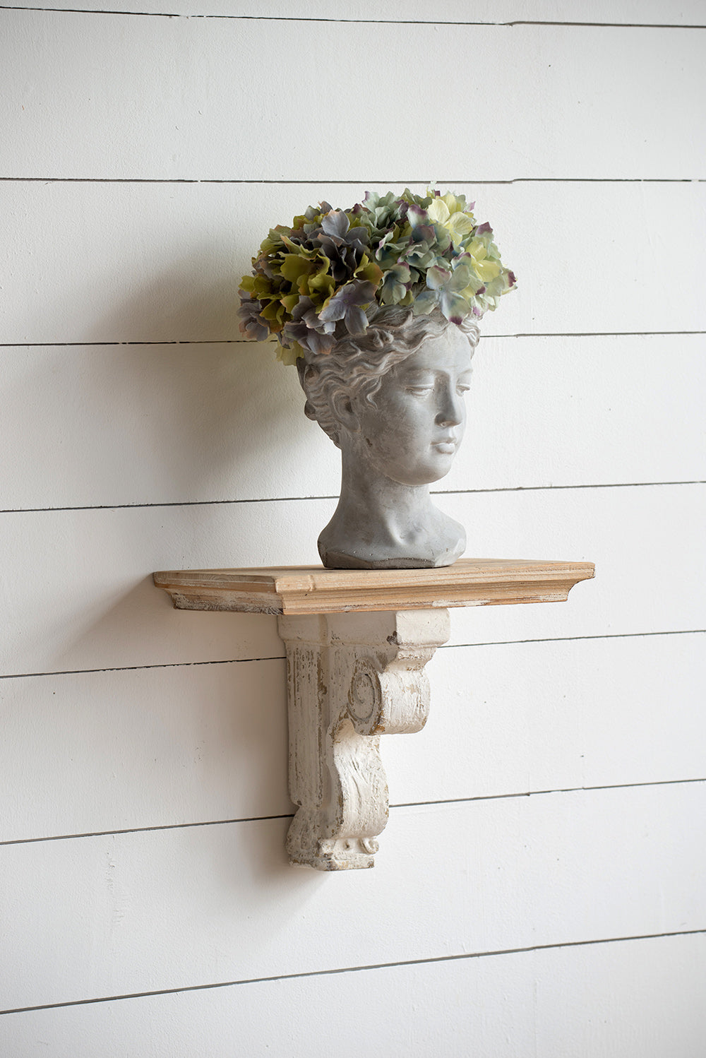 Gray bust planter holding muted green hydrangeas on distressed wooden shelf