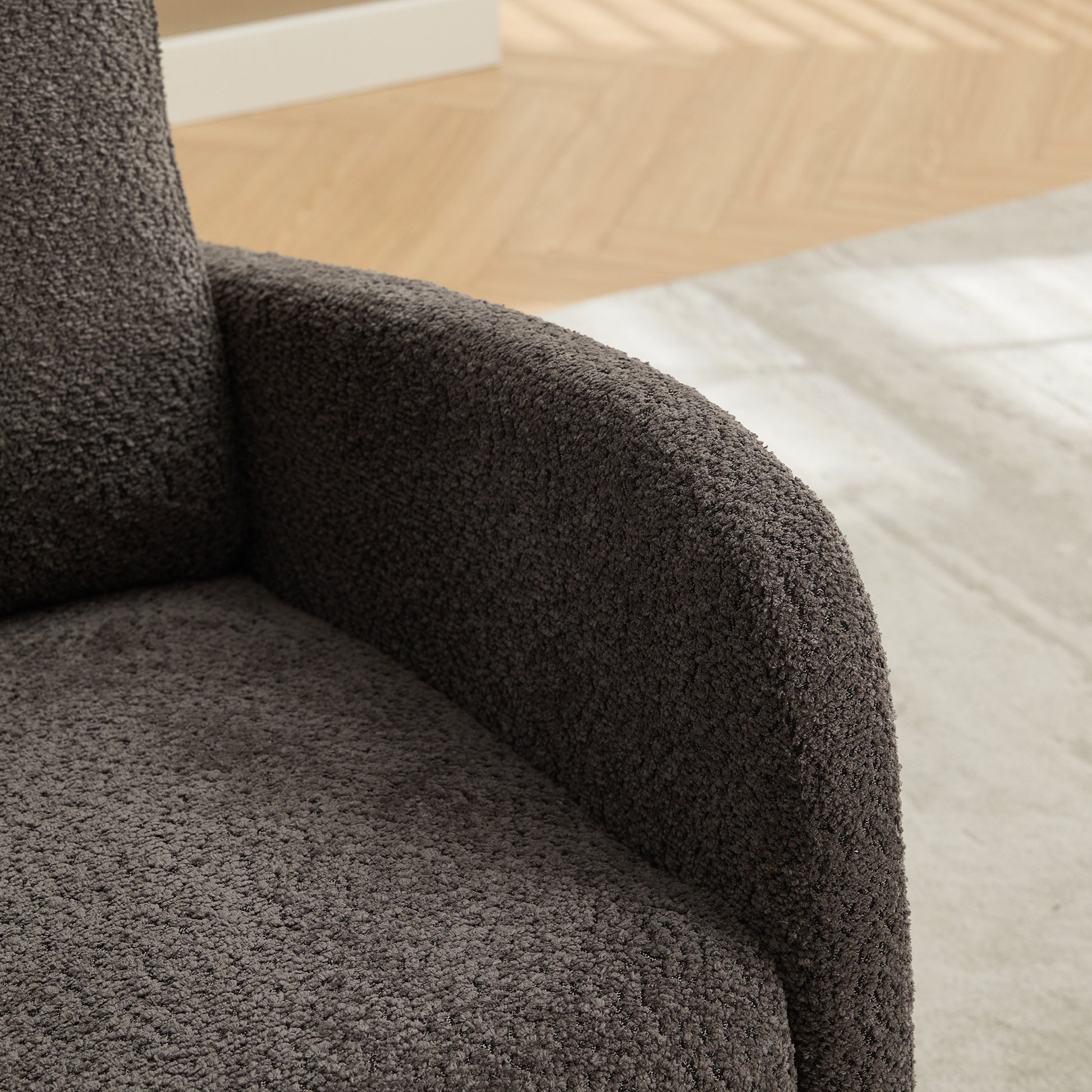 Closeup of a plush dark gray armchair armrest with textured fabric