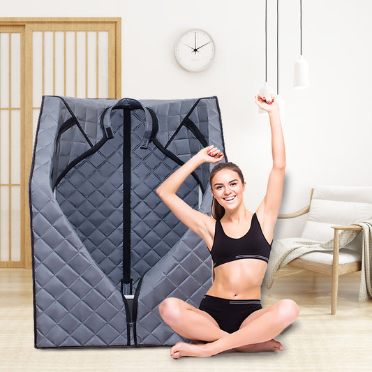 Gray quilted portable steam sauna tent with a woman stretching happily beside it