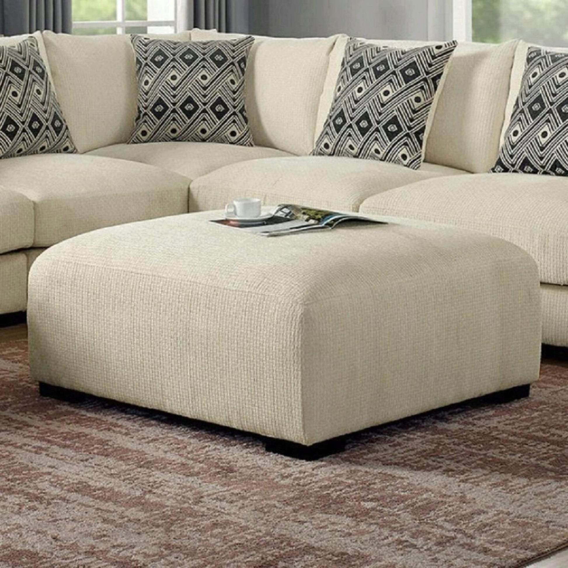 Cream textured fabric ottoman with a magazine and cup on top perfect for living room decor