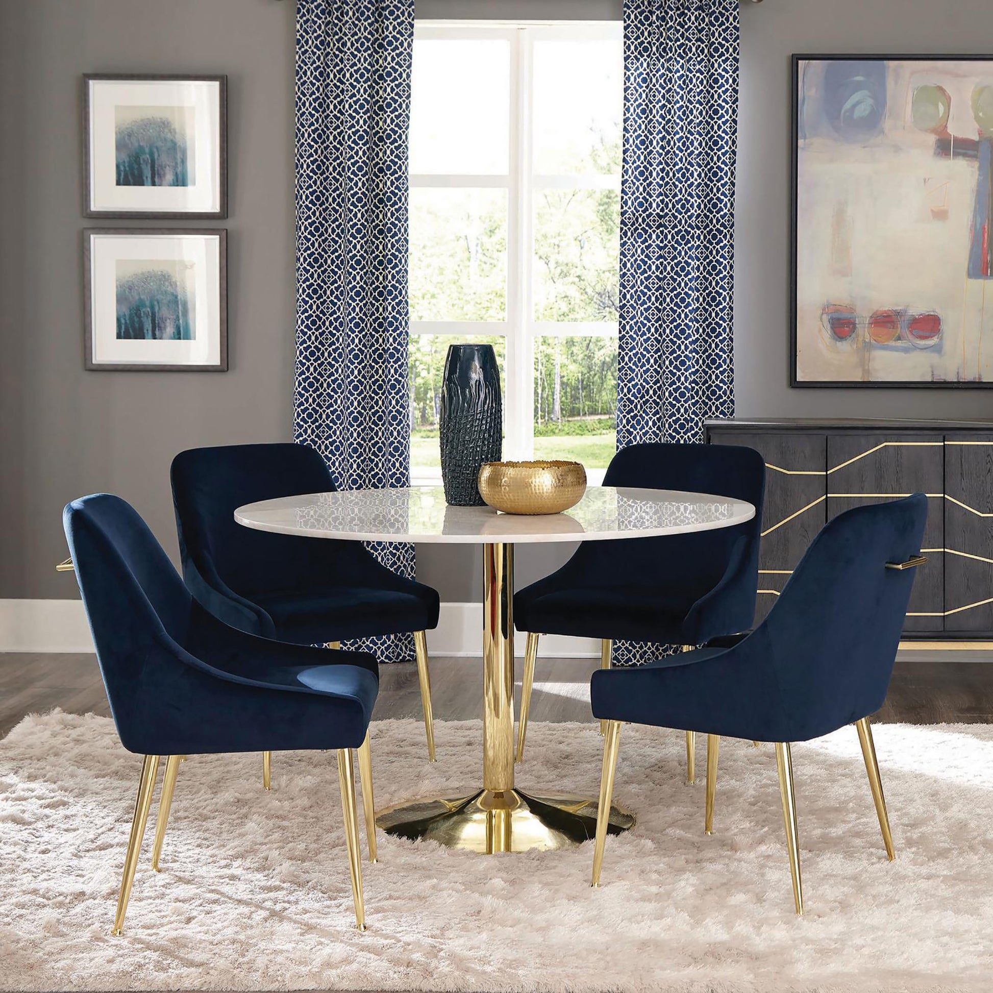 Four navy velvet dining chairs with gold legs around a white marble top pedestal table