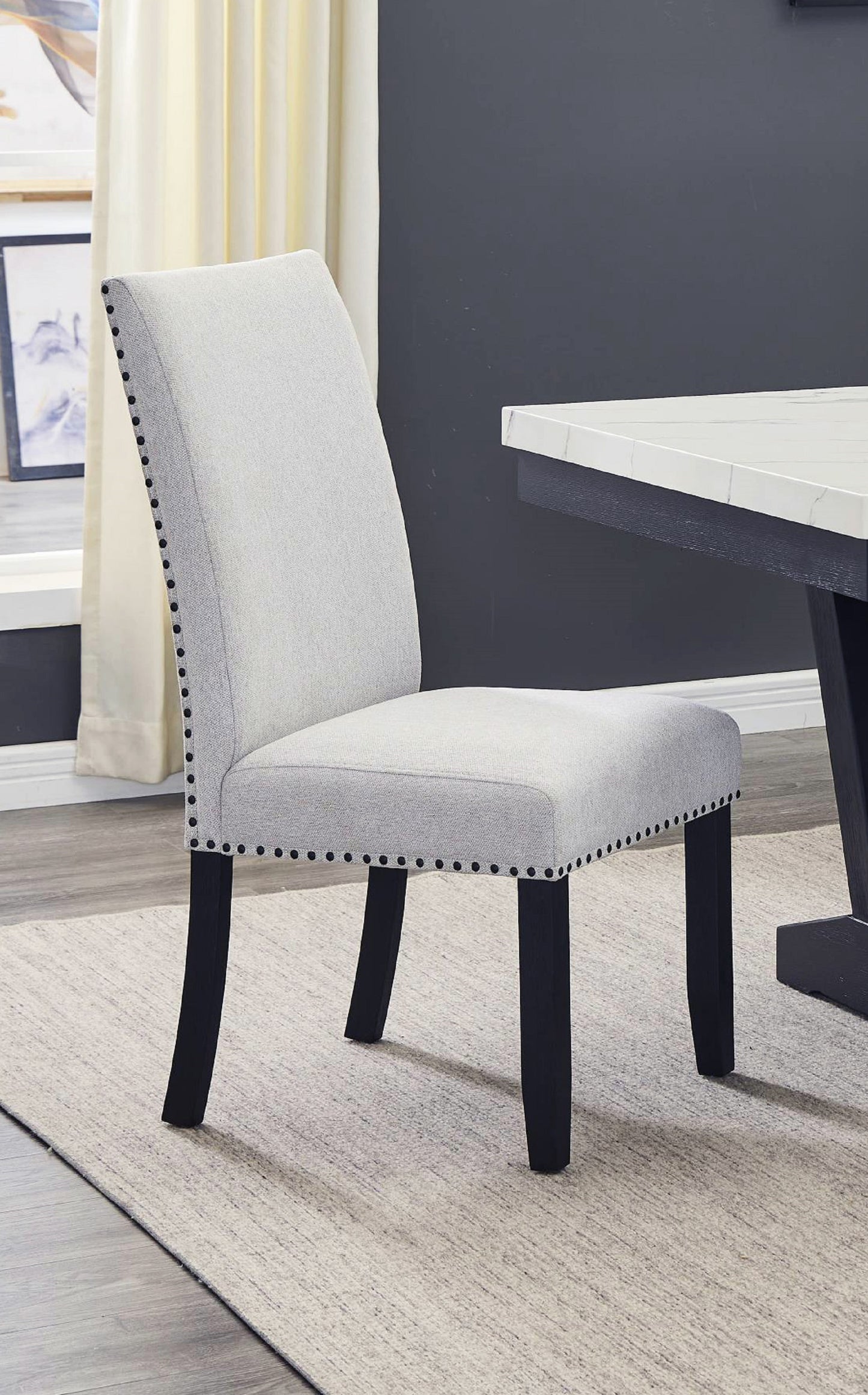 Upholstered dining chair in light gray fabric with black nailhead trim and dark wood legs
