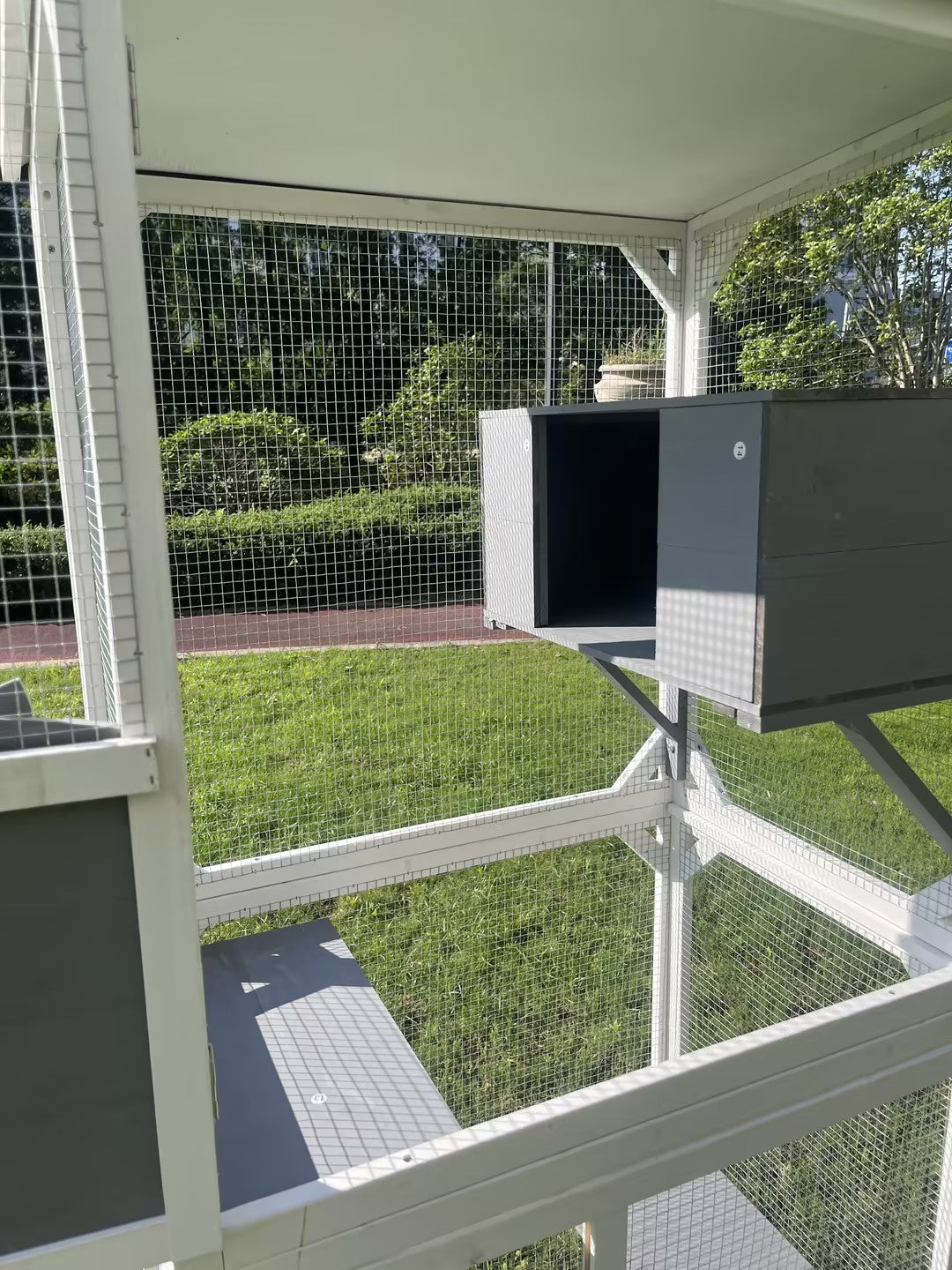 Wooden outdoor catio with gray sleeping box and grass backdrop