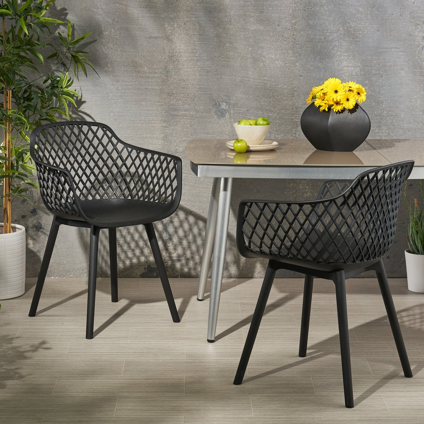 Two black modern outdoor chairs with a diamond pattern seating on a patio