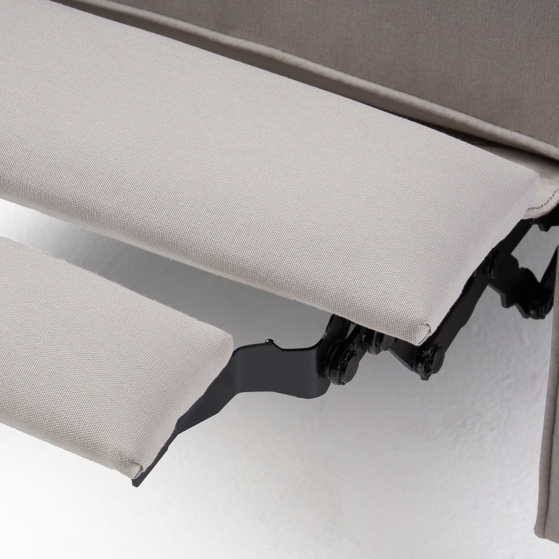 Closeup of beige fabric recliner footrest mechanism with black metal support