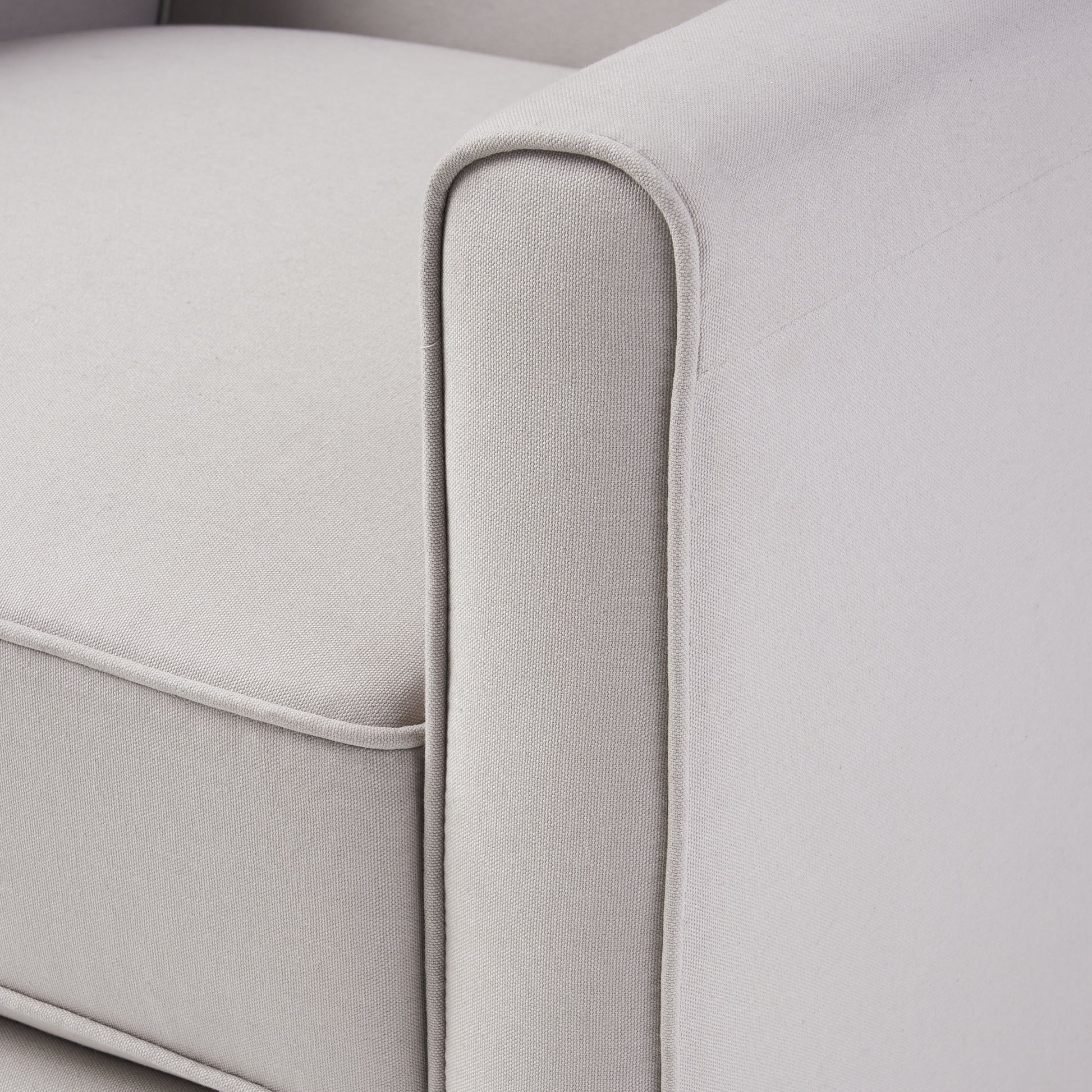 Closeup of a light gray fabric armchair armrest with piped detailing