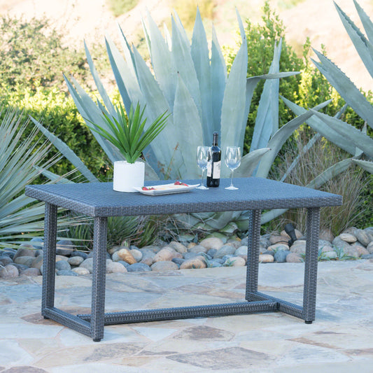 Gray wicker outdoor dining table with two wine glasses and a bottle of wine