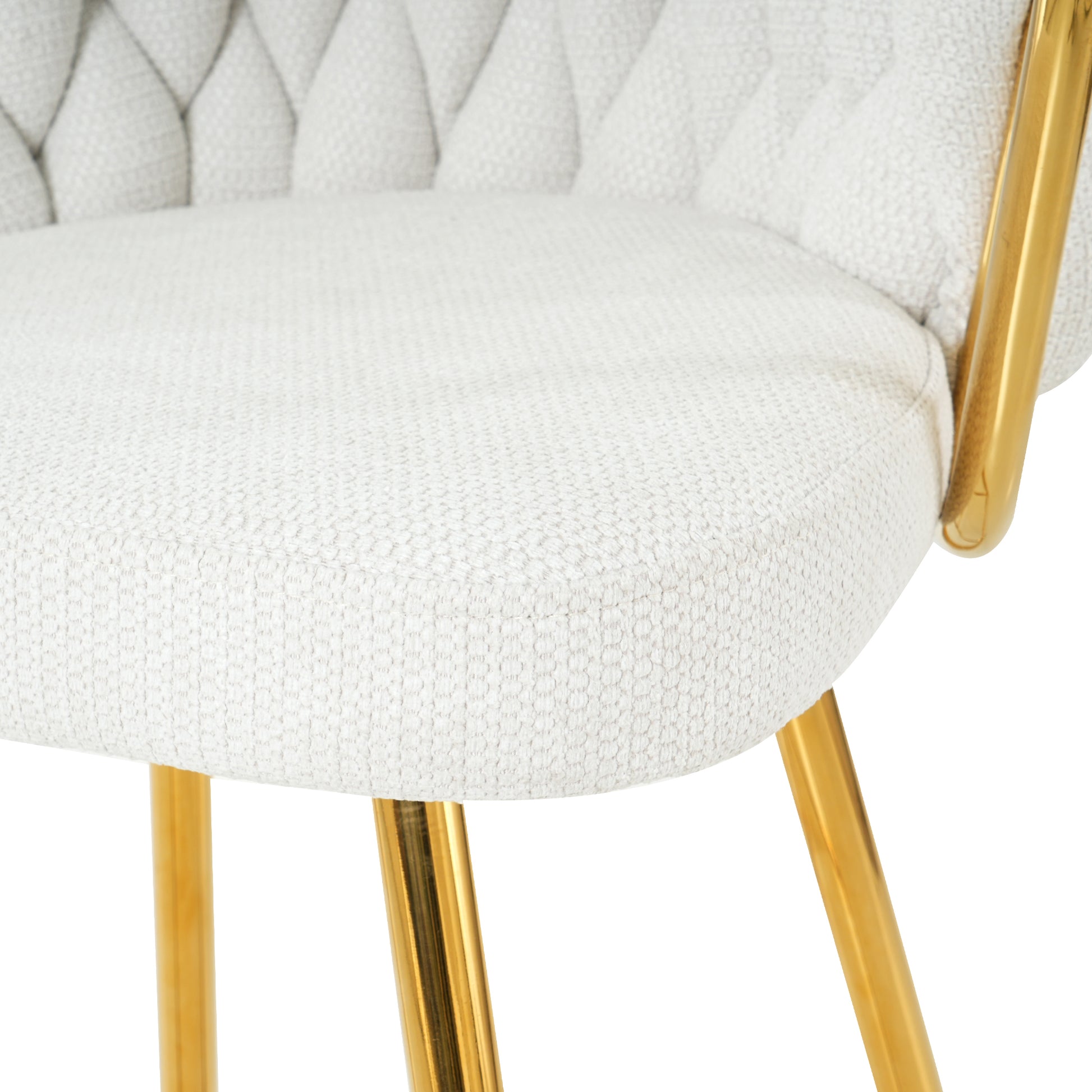 Closeup of a tufted ivory fabric armchair with polished gold metal legs