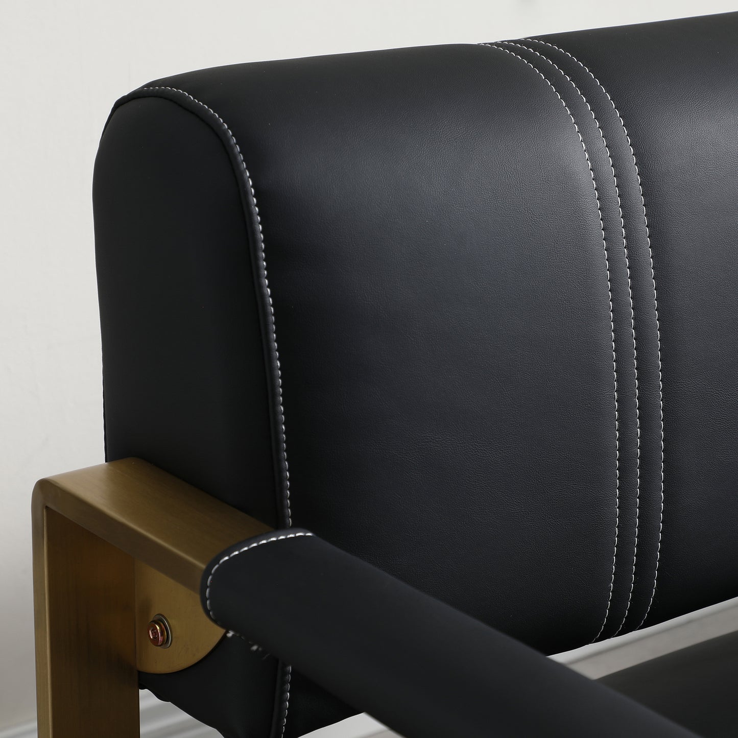 Black faux leather armchair with white stitching and gold metal frame