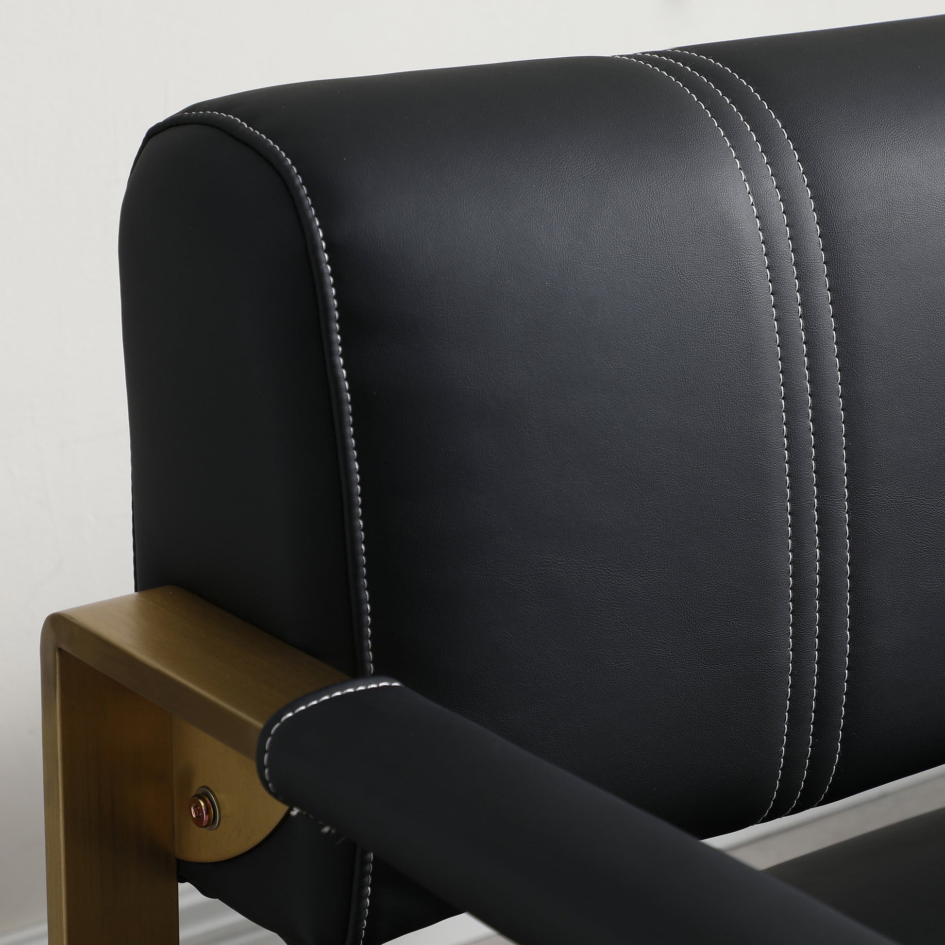 Black faux leather armchair with white stitching and gold metal frame