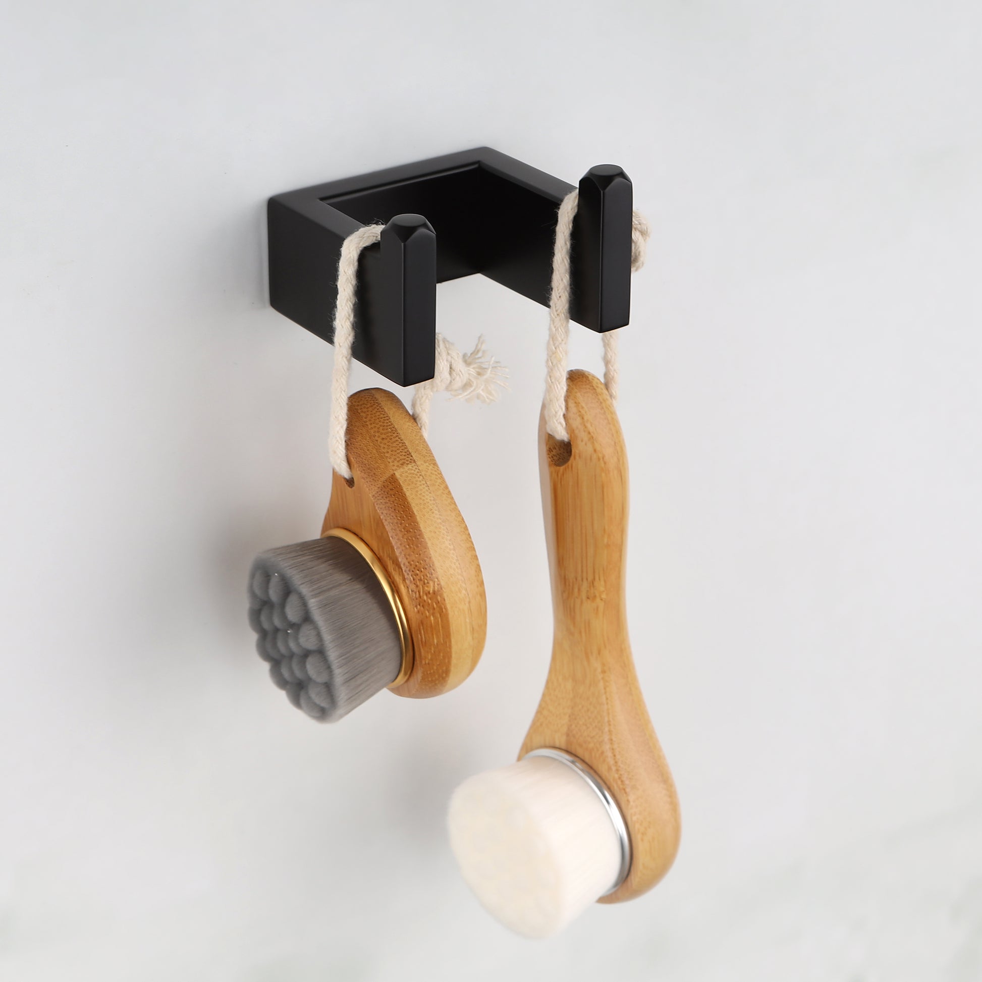 Two bamboo facial cleansing brushes with white bristles hang from a black wall hook