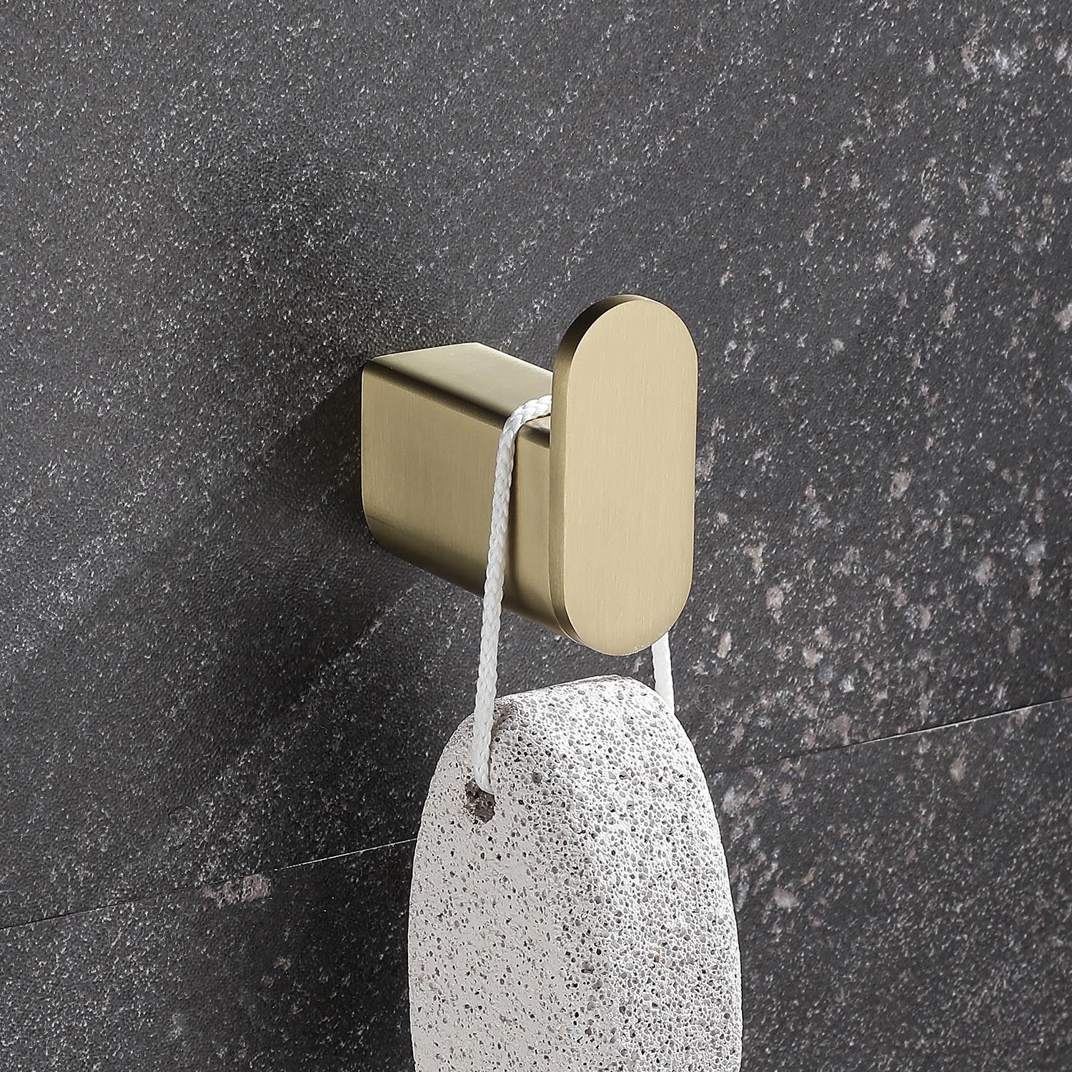 Brushed gold bathroom hook holding a pumice stone with a white rope loop