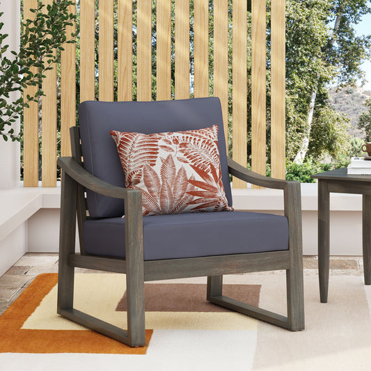 Gray wooden outdoor armchair with dark gray cushions and patterned accent pillow