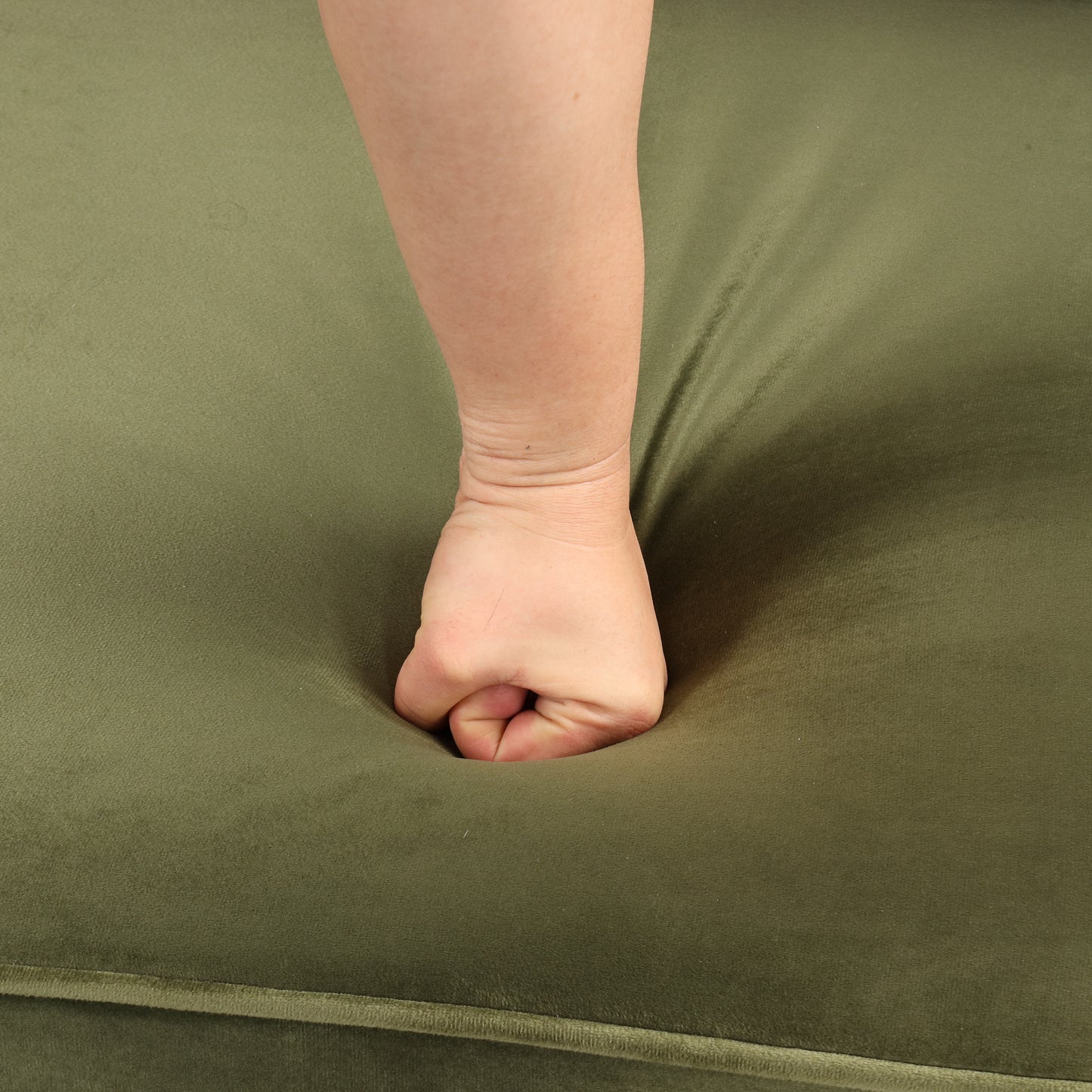 Closeup of a hand pressing into plush olive green velvet upholstery showing depth and comfort