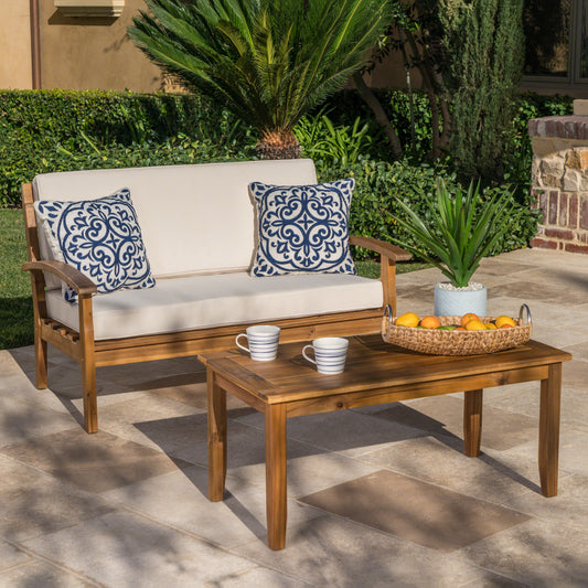 Acacia wood patio loveseat with plush beige cushions and blue patterned outdoor pillows