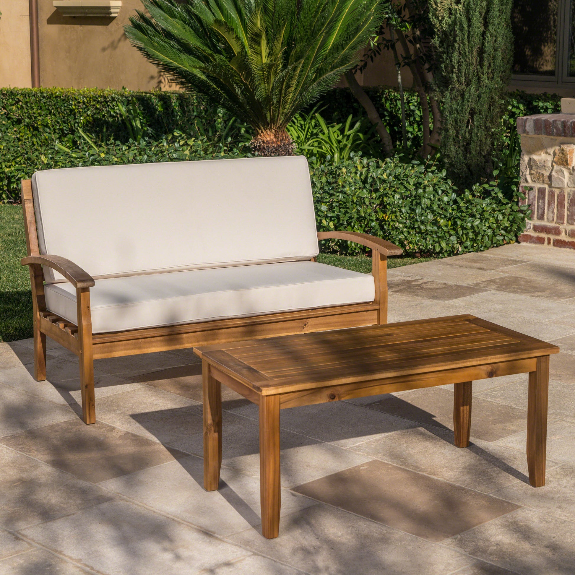 Natural wood outdoor loveseat with cream cushions and matching coffee table