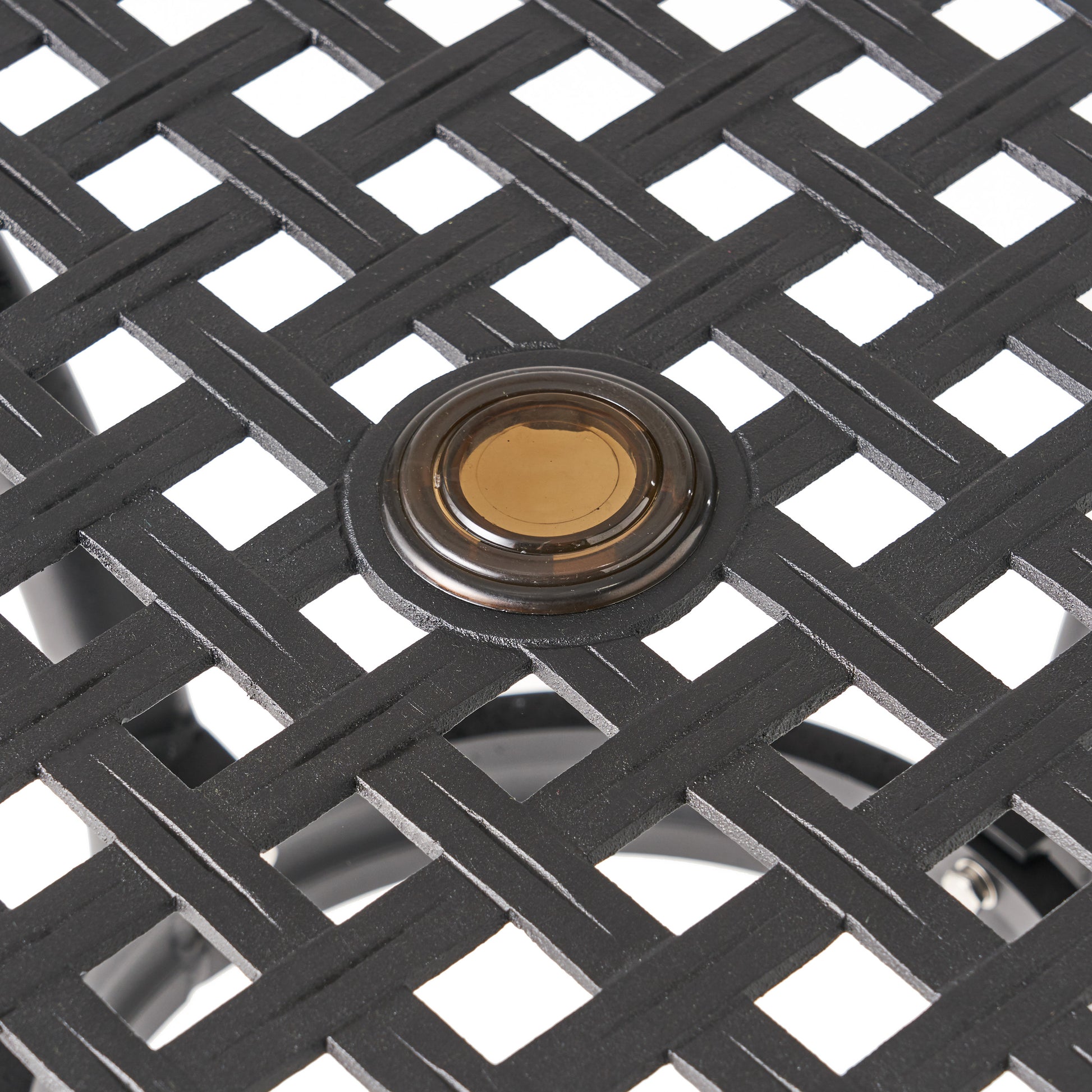 Closeup of black metal table surface with woven design and amber glass accent