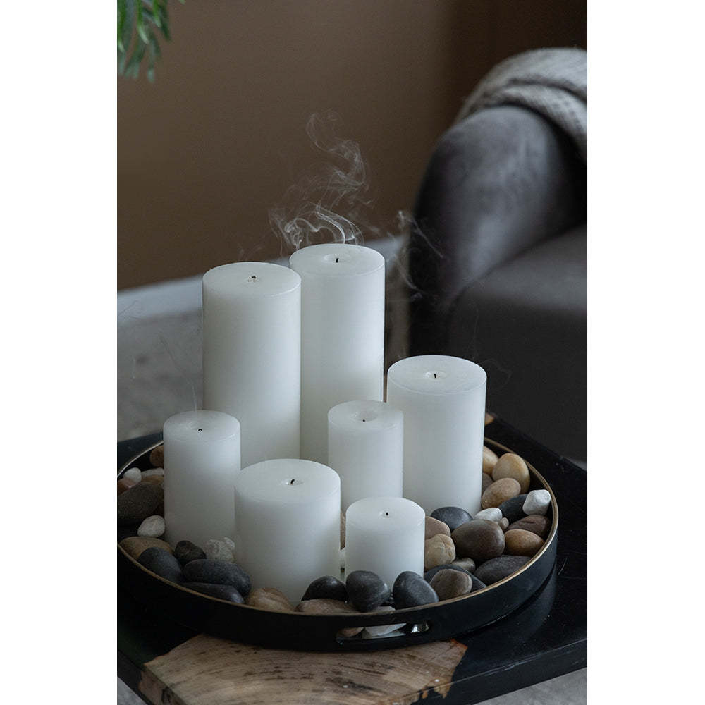 Set of six white pillar candles of varying heights arranged on river stones in a black tray