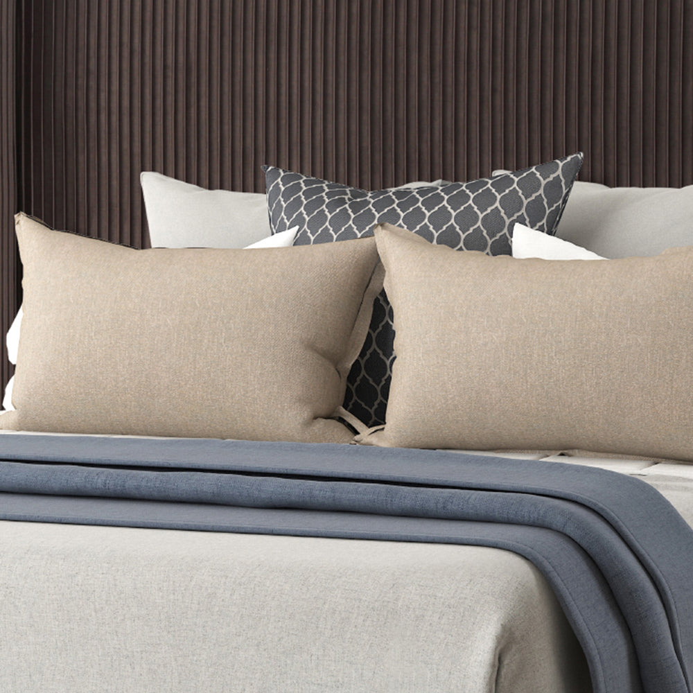 Set of two beige linen throw pillows on a bed with a grey geometric accent pillow