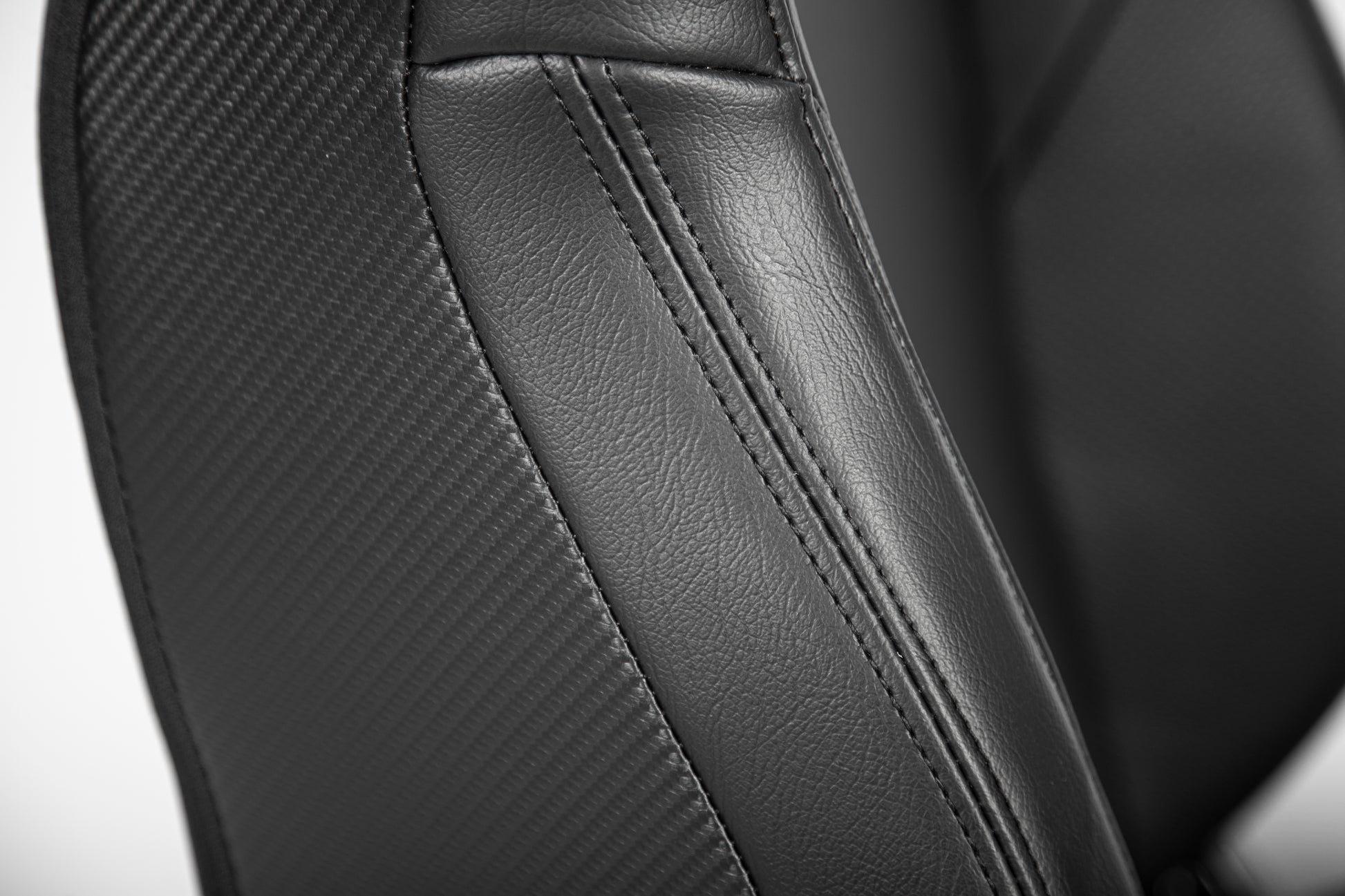Closeup of black gaming chair seat featuring carbon fiber texture panel and stitched faux leather