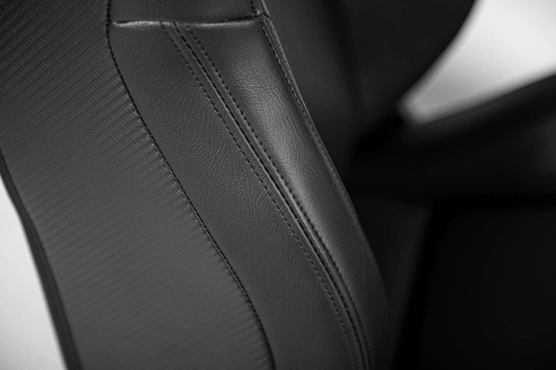 Black leather car seat upholstery with carbon fiber texture and contrast stitching detail