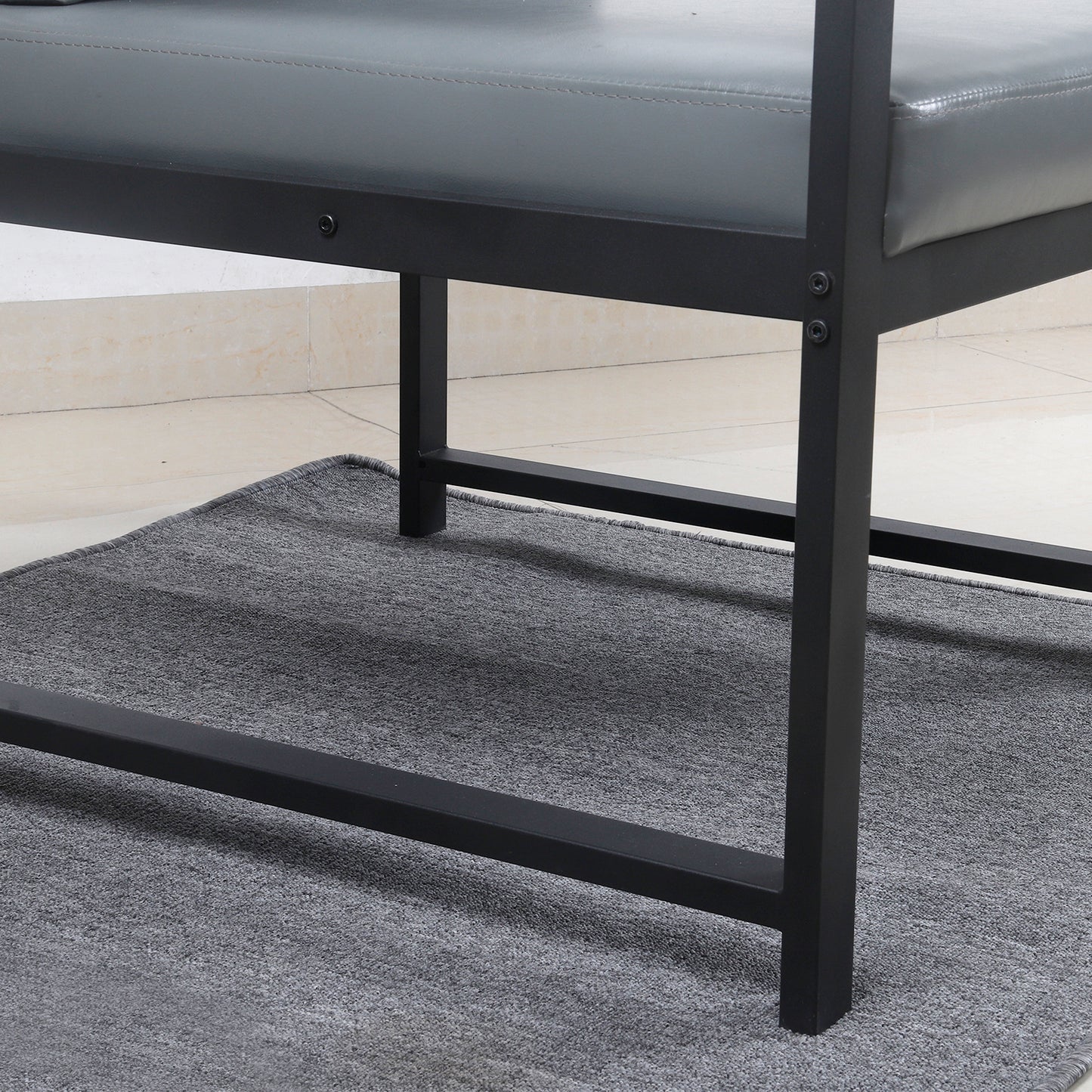 Closeup of gray faux leather bench seat with black metal frame legs on a textured rug